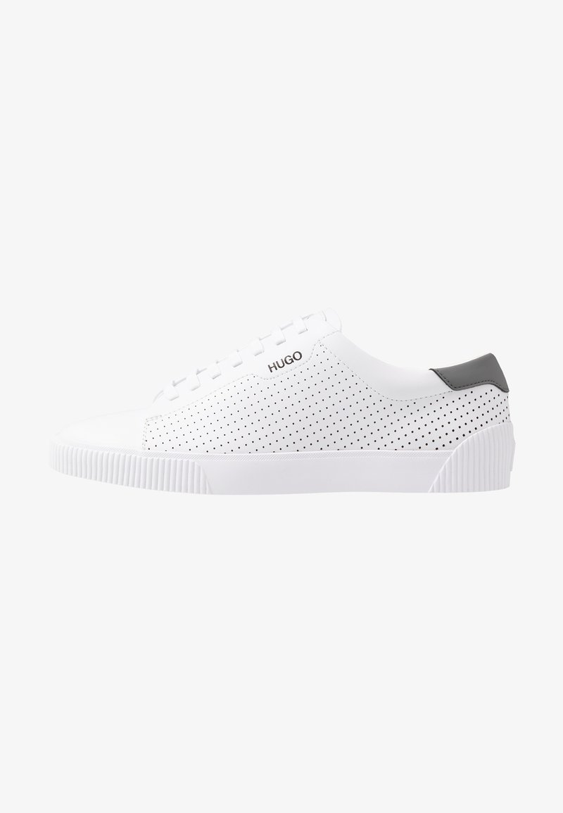 Baskets basses blanches avec côtés perforés, languette de talon noire, semelle en caoutchouc blanche et logo "HUGO" près des lacets.