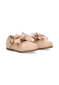 Zapatos de gamuza beige de tamaño infantil con suelas marrones, grandes lazos de satén y correas laterales ajustables sobre un fondo blanco.
