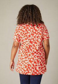 Túnica roja con estampado floral blanco, de mangas cortas y un corte holgado, combinada con pantalones azul oscuro. Material de algodón, textura suave.