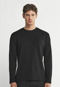 Svart långärmad t-shirt i mjukt tyg med rund halsringning. Minimalistisk design utan synliga logotyper eller mönster. Rak passform.