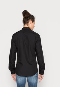 Camicia nera a maniche lunghe con taglio dritto, caratterizzata da un colletto, polsini abbottonati e tessuto liscio, indossata con jeans blu.