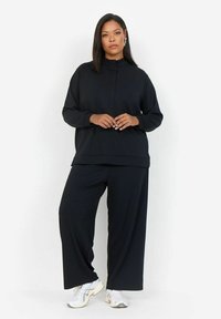 Sudadera negra de corte holgado con cuello alto y mangas largas, combinada con pantalones de pierna ancha. Hecha de una tela suave y lisa.