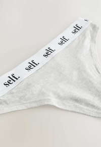 Sivi stringi od mekog materijala, sa bijelom elastičnom gumom na struku na kojoj piše "self." u crnoj boji, ravnim šavovima i jednostavnim dizajnom.