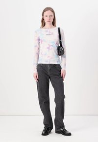 Dugih rukava, lagana majica od prozirnog materijala s višebojnim tie-dye uzorkom. Uparen s tamnosivim širokim trapericama i crnim cipelama.