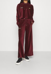 Bordeaux velours loungewear set bestaande uit een cropped hoodie en losse broek, beide met kleine logo-accenten en trekkoorddetails.