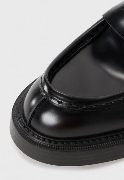 Zwarte leren loafers met een glanzende afwerking, ronde neus, subtiele stikdetails en een geprofileerde zwarte rubberen zool.