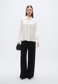 White, long-sleeve, button-up blouse paired with black, wide-leg trousers. The outfit features a smooth texture and a clean design.