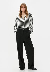 Camisa de rayas blancas y negras de manga larga combinada con pantalones negros de cintura alta y un cinturón negro con una hebilla circular de plata.