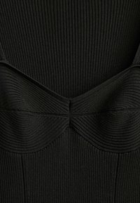 Gros plan d'un tissu tricoté côtelé noir avec un détail de couture courbe créant un élément de design structuré et sculpté sur le vêtement.
