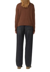 Brauner Strickpullover mit rundem Ausschnitt, geripptem Saum und Rückennaht, kombiniert mit locker sitzenden dunkelgrauen Denim-Jeans und beigen Schuhen.