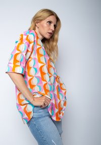 Koszula krótko rękawowa z geometrycznym wzorem w kolorach różowym, pomarańczowym, turkusowym i kremowym, wykonana z lekkiego materiału o luźnym kroju.