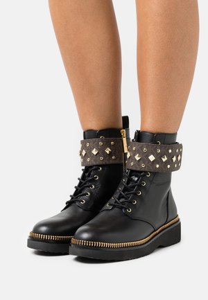 Černé kotníkové boty z kůže s manžetou z tkaniny ozdobenou nýty, zlat tónovaným kováním, zaoblenou špičkou a texturovanou gumovou podrážkou s dekorativním zipem.