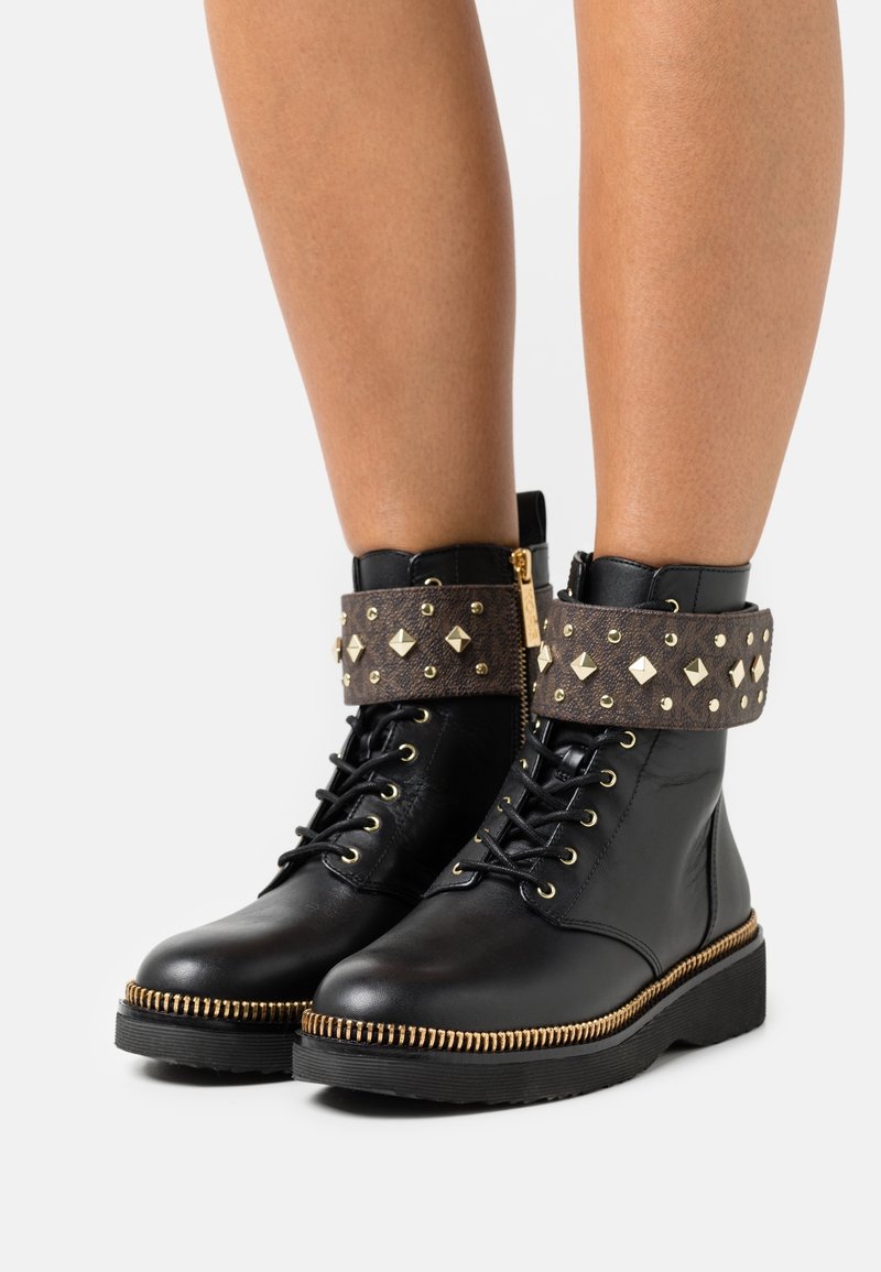 Czarne skórzane botki za kostkę z mankietem z materiału ozdobionym ćwiekami, złotymi elementami metalowymi, zaokrąglonym noskiem oraz teksturowaną gumową podeszwą z ozdobnym zamkiem błyskawicznym.