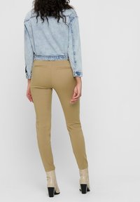 Avskuren denimjacka i ljusblått tyg, med sömnadsdetaljer på baksidan, kombinerad med beige slim-fit-byxor och texturerade beigefärgade högklackade stövlar.