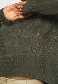Groene gebreide trui met verschillende texturen, geribde manchetten en een cropped ontwerp, aangevuld met een relaxed pasvorm.