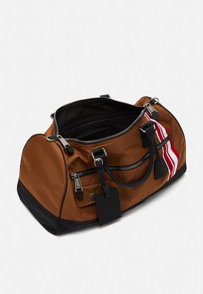 Brown nylon duffel bag with black accents, zippered closure, dual handles, and red-white striped detail on one side. Interior is black.
