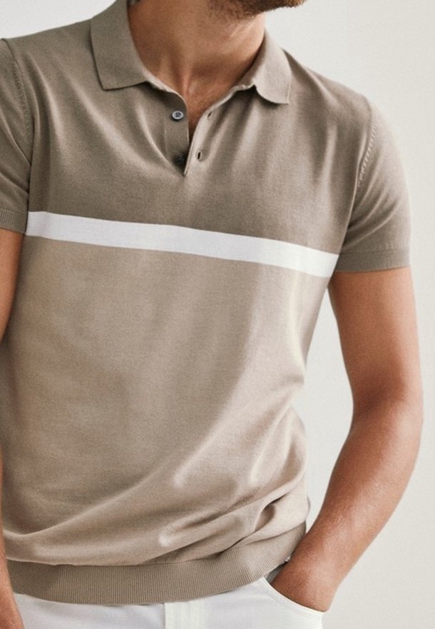 Homme portant un polo beige à manches courtes avec une bande horizontale blanche et un pantalon blanc, main posée négligemment dans la poche.