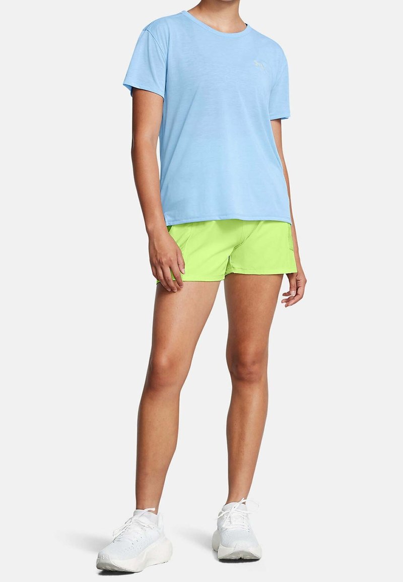 Camiseta de manga corta azul claro, con un corte relajado, combinada con shorts verdes brillantes. Zapatillas deportivas blancas completan el look deportivo.