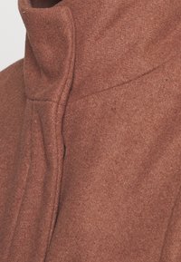 Abrigo de lana marrón con un alto cuello y líneas limpias, de textura suave y sin cierres visibles ni patrones.