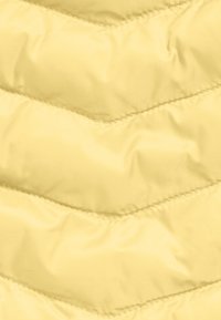 Tessuto trapuntato giallo pallido con un motivo a zigzag e cuciture visibili che creano una texture imbottita.