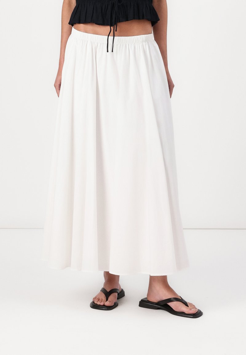 Larga falda blanca con cinturilla elástica, hecha de tejido ligero, presenta un diseño fluido y una textura suave. Combinada con sandalias negras de dedo.