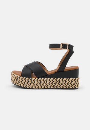 Sandales à plateforme en cuir noir avec des accents en paille tissée, bride de cheville avec boucle, et une semelle épaisse et texturée pour plus de stabilité.
