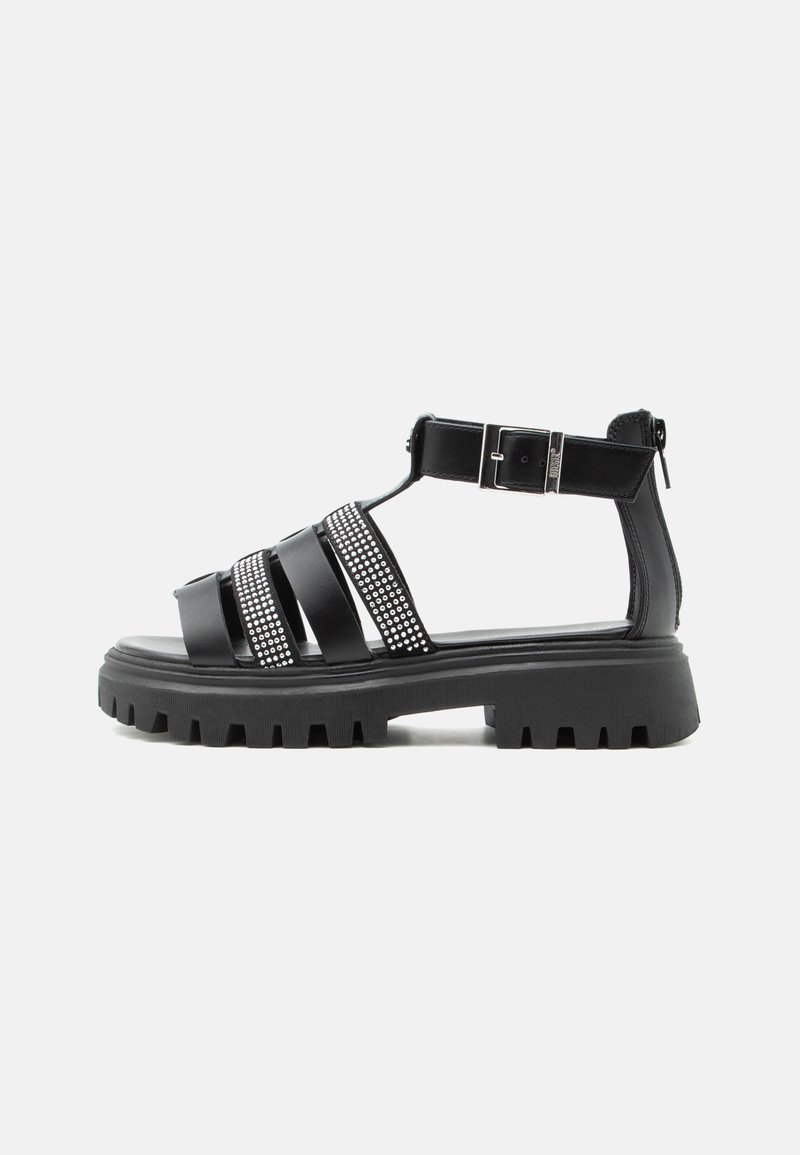 Μαύρο σανδάλι με παχύ πάτο και πολλές λουρίδες, διακόσμηση με στρας, αγκράφα στον αστράγαλο και φερμουάρ στο πίσω μέρος, εμφανιζόμενο σε λευκό φόντο.