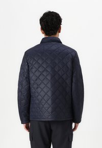 Jachetă cu model căptușit în nuanță de navy, cu un model de diamante, având guler și mâneci lungi. Material neted și strălucitor. Design simplu, fără embellishments.
