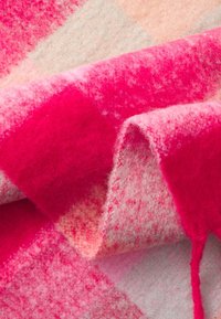 Tissu en laine douce à motif à carreaux rose et pêche, plié pour montrer la texture et le contraste de couleurs vives.