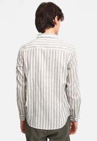 Camicia di lino a righe in beige chiaro con righe grigie, maniche lunghe, polsini con bottoni e orlo arrotondato. Presenta una sottile trama e un colletto.