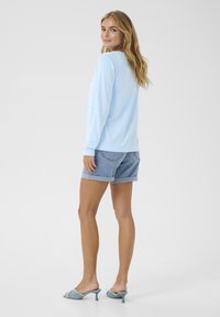 Lichtblauw shirt met lange mouwen, gecombineerd met denim shorts en blauwe haksandalen. Het shirt heeft een ronde halslijn en een losse pasvorm.