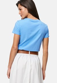 T-shirt court bleu clair en coton doux, avec des manches courtes et un col rond, associé à une jupe blanche et une ceinture marron.