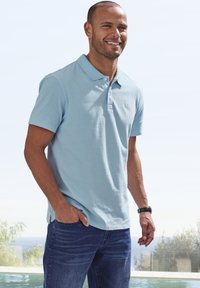 Polo shirt à col bleu clair à manches courtes, en tissu lisse. Assorti à un jean en denim foncé, affichant une coupe décontractée.