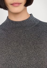 Pull en col roulé noir avec un motif tricoté texturé et métallique, doté d'un col ajusté et d'une coupe près du corps.