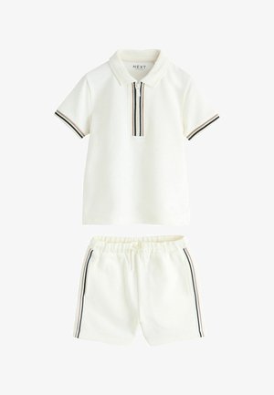 Tricou polo alb cu mâneci scurte, fermoar frontal și tiv cu dungi, asortat cu pantaloni scurți albi cu talie elastică și dungi laterale asortate.
