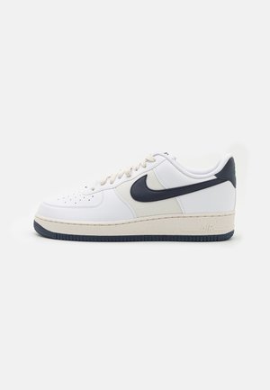 Sneakers bianchi in pelle con accenti blu navy, pannelli in rete testurizzata e suole crema. Presentano una punta forata e il logo "AIR" sul tallone.