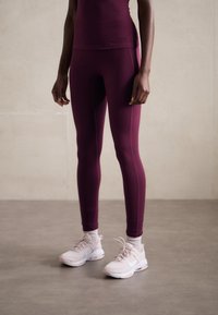Burgundy idrottströja och leggings gjorda av stretchigt material, i kombination med ljusrosa sneakers. Slät textur och åtsittande design.