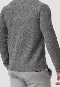 Maglione grigio tricot con finitura texturizzata, scollatura rotonda e maniche lunghe. Orlo leggermente curvato e un dettaglio di cucitura visibile nella parte inferiore.