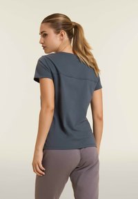 Camiseta de algodón gris de manga corta, con un sutil detalle de costura en la parte posterior, combinada con pantalones de chándal lilas claros.
