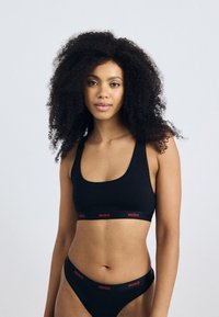Svart BH og matchende bikini-truse, begge med en rød "HUGO" logo-bånd. Glatt stoff, minimalistisk design, tettsittende fasong.