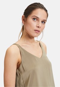 Khaki mouwloos shirt met een V-hals ontwerp, een gladde textuur en een minimalistische stijl zonder extra versieringen.