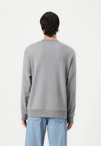 Felpa grigia con maniche lunghe, scollo rotondo, cinturini e orlo a coste, realizzata in tessuto morbido, abbinata a jeans baggy blu chiaro.