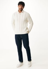 Pull en tricot blanc épais avec un col haut et deux boutons en bois ; assorti à un jean bleu foncé et des baskets blanches.