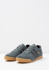 Sneakers in suede grigio con strisce nere e logo dorato. Punta arrotondata, suola in gomma testurizzata e chiusura con lacci.