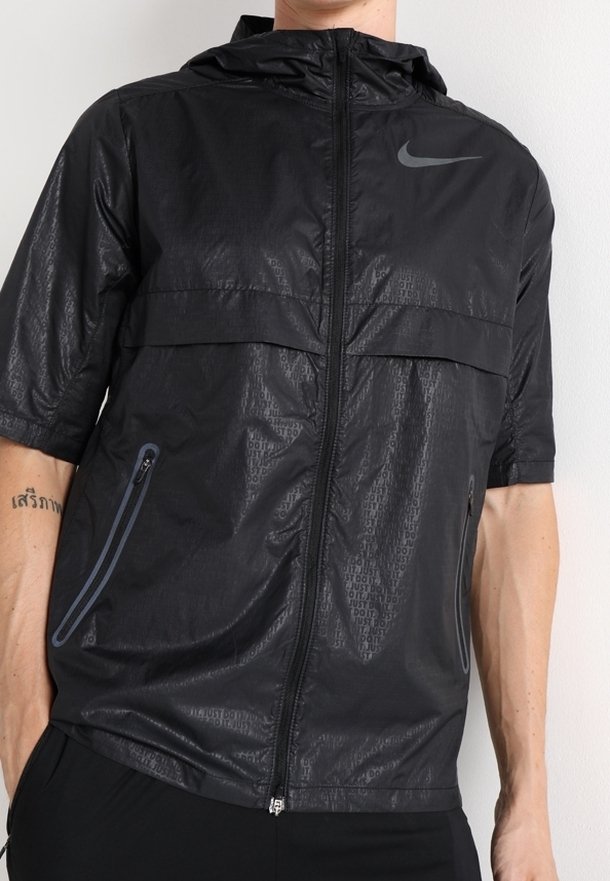 Veste Nike noire à manches courtes avec capuche, fermeture éclair frontale, poches zippées et motif subtil "Just Do It" sur le tissu.