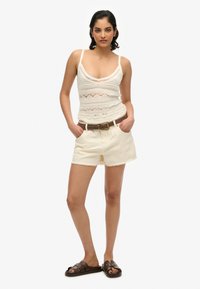 Top de tirantes blanco de crochet con escote bajo, combinado con pantalones cortos color crema con bordes deshilachados y un cinturón marrón. Sandalias planas marrones.