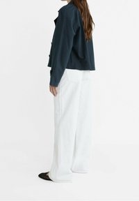 Granatowa kurtka o luźnym kroju, z guzikami, zestawiona z białymi spodniami o wysokim stanie i szerokimi nogawkami oraz czarnymi balerinami. Gładka struktura tkaniny.