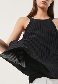 Zwarte geplooide mouwloze top met een gestructureerde stof, voorzien van een hoge halslijn en een uitlopende zoom die een sierlijke val creëert.