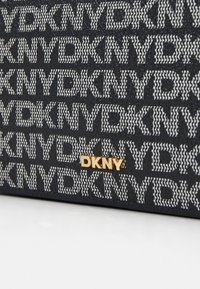 Peníze DKNY s černým textilním povrchem, na kterém se opakuje bílý text a zlatý logový detail. Texturovaná rozložení s pevnými tvary.