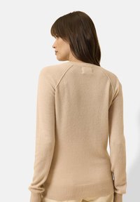 Beiger Strickpullover mit taillierter Passform, gerippten Bündchen und Saum sowie Rundhalsausschnitt. Glatte Textur mit Raglanärmelkonstruktion.